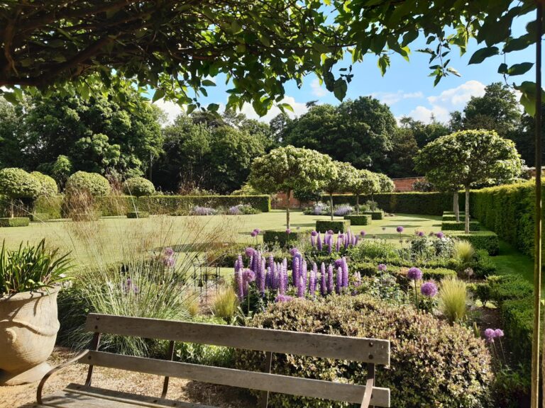 A stunning walled garden featuring manicured main lawn flowerbeds and striking Catalpa trees.